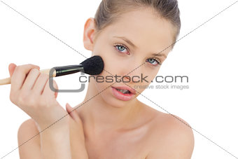 Serious brunette model applying powder on her cheek