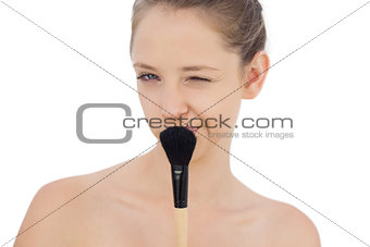 Playful brunette model holding a brush and winking at camera