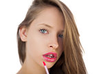 Serious brunette model applying pink gloss on her lips
