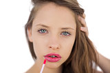 Calm brunette model applying pink gloss on her lips