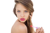 Thoughtful brunette model applying gloss on her lips