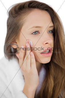 Thoughtful brunette in bathrobe rubbing her cheek with cream