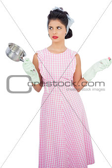 Puzzled black hair model holding a pan and wearing rubber gloves