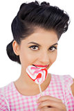 Cheerful black hair model chewing a heart shaped lollipop