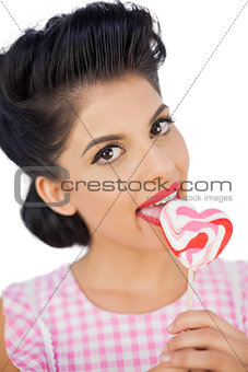Cheerful black hair model licking a heart shaped lollipop