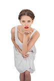 Unsmiling model in white dress blowing a kiss at camera