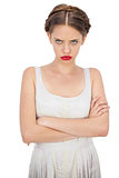 Frowning model in white dress posing with crossed arms