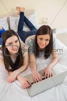 Friends using a laptop lying on bed and smiling at camera