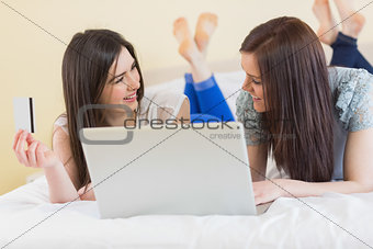 Pretty friends using a laptop to shop online lying on bed