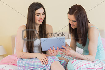 Smiling friends in pajamas talking on bed using a tablet