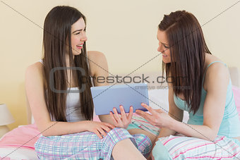 Happy friends in pajamas talking on bed using a tablet
