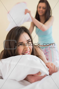 Cheerful friends in pajamas having a pillow fight on bed