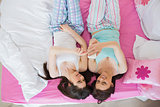 Pretty friends in pajamas looking at smartphone on bed