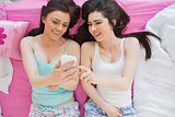 Cheerful friends in pajamas looking at smartphone on bed
