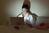 Pretty teen wearing bathrobe using her laptop in the dark