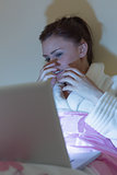 Pretty teen wearing dressing gown watching a scary movie on laptop