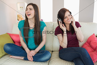 Girl listening to music with her friend beside her on the sofa