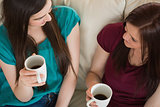 Two smiling friends having coffee and chatting on the couch
