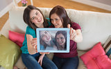 Two smiling friends on the couch taking a selfie with tablet pc