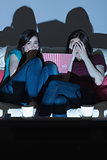 Two friends on the couch watching a scary movie together in the dark