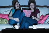 Two laughing friends on the couch watching tv together in the dark