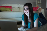 Smiling brunette lying on floor using laptop in the dark