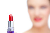 Nude blonde model holding red lipstick on foreground