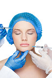 Surgeons making injection on peaceful blonde wearing blue surgical cap