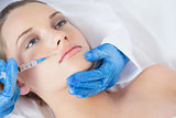 Surgeon making injection above lips on young woman lying