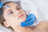 Surgeon making injection on forehead on young woman lying