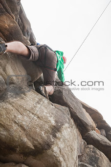 Determined man climbing a large rock face and seeing the summit
