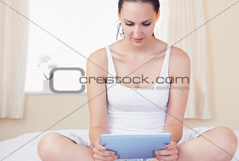 Content brunette sitting on bed using her tablet pc
