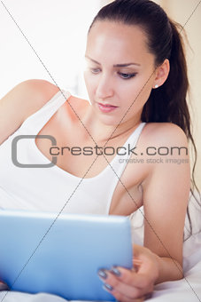 Calm brunette lying on bed using her tablet pc