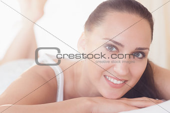 Smiling brunette lying on bed looking at camera