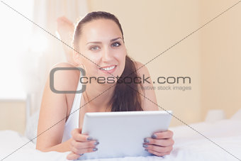 Happy brunette lying on bed with her tablet pc
