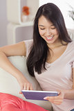Pretty asian girl using her tablet on the couch