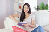 Happy asian girl using her tablet on the couch looking at camera