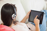 Girl using her tablet pc on the couch and listening to music