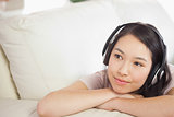 Pretty asian girl lying on the sofa and listening to music