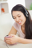 Relaxing asian girl lying on the sofa and listening to music with smartphone
