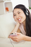 Happy asian girl lying on the sofa and listening to music with smartphone