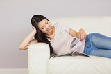 Cheerful asian girl lying on the sofa reading a magazine