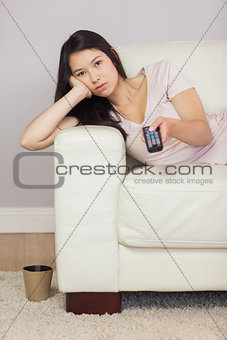Bored asian girl lying on the sofa watching tv