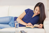 Happy asian girl lying on the sofa reading a novel