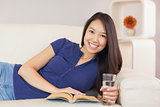 Beautiful asian girl lying on the sofa reading a novel and drinking water