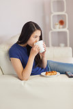 Woman sitting on the sofa drinking coffee with a pastry