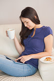Young asian woman using her tablet pc and holding mug of coffee