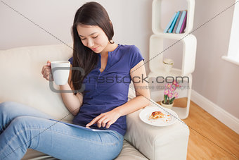 Young smiling asian woman using her tablet pc and holding mug of coffee