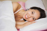 Happy young asian woman lying in her bed smiling at the camera