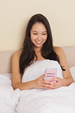 Young asian woman sitting in bed using smartphone